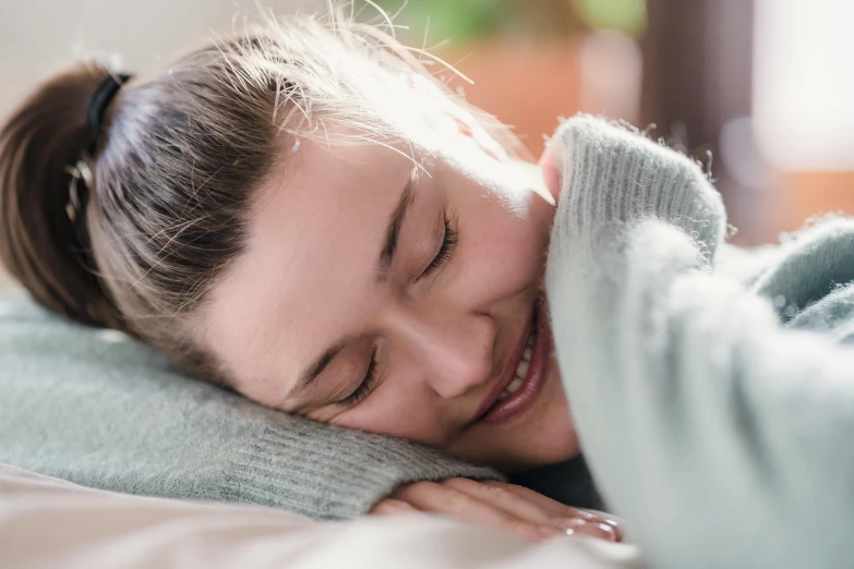 a woman laying on top of a bed next to a pillow, by Alice Mason, trending on pexels, smiling laughing, close up of face, cuddling, acupuncture treatment