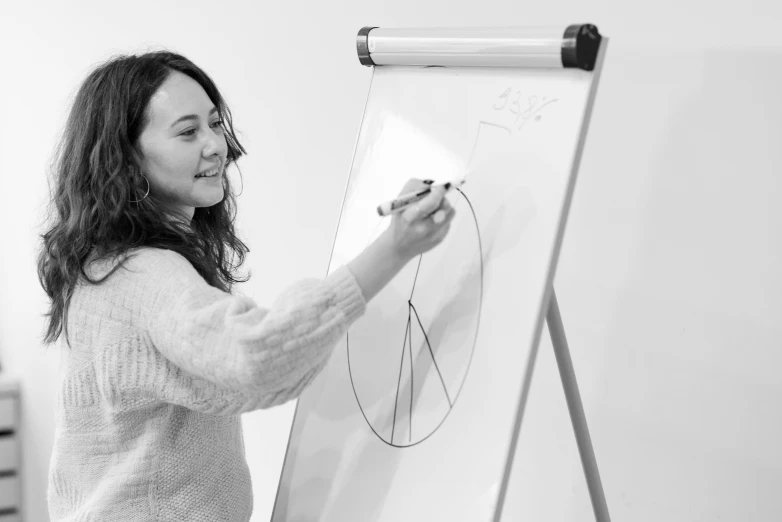 a black and white photo of a woman writing on a white board, a drawing, joy ang, proportions on a circle, professional illustration, teaching