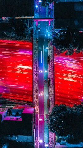 an aerial view of a city at night, an album cover, unsplash contest winner, futurism, red car, rainbow road, symmetrical image, giant red led screens
