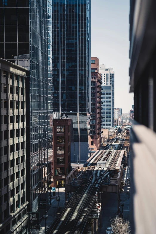 a train traveling through a city next to tall buildings, pexels contest winner, location [ chicago ( alley ) ], high view, rail tracks, stacked image