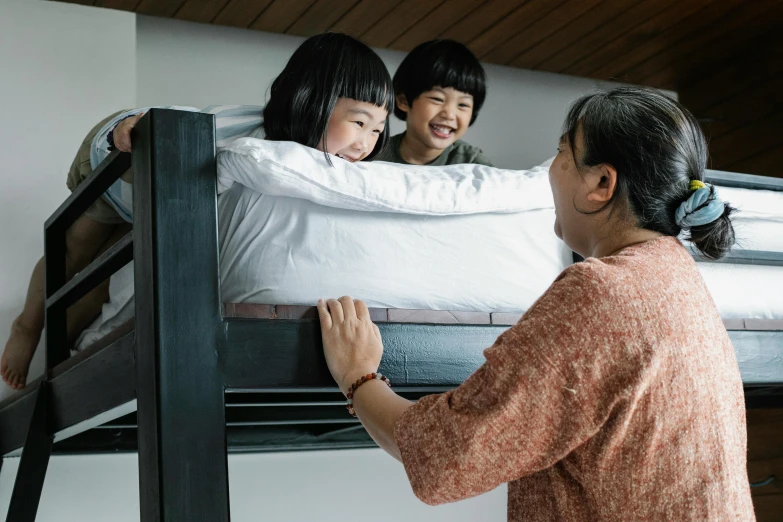 a woman placing a pillow on top of a bunk bed, inspired by Okada Hanko, pexels contest winner, mingei, happy family, singapore, looking at each other mindlessly, with a kid