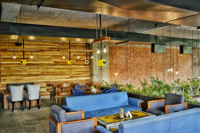 a blue couch sitting in a living room next to a wooden wall, cafe tables, indiecraft aesthetic, thumbnail, open ceiling