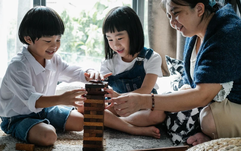 a woman and two children playing with wooden blocks, pexels contest winner, asian features, tabletop game board, towering, grown up