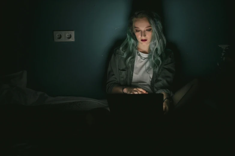 a woman sitting in front of a laptop computer, inspired by Elsa Bleda, trending on pexels, spooky netflix still shot, dark green hair, in the bedroom at a sleepover, gray skin. grunge