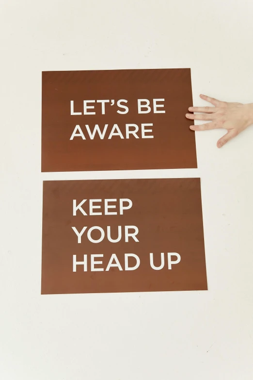 a person holding a sign that says let's be aware keep your head up, a screenprint, reddish - brown, pair of keycards on table, rear facing, bronze