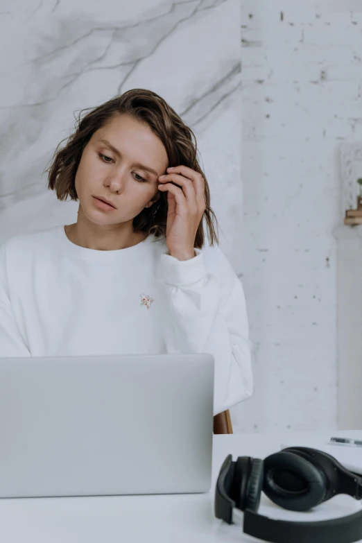 a woman sitting at a table with a laptop and headphones, trending on pexels, wearing a white sweater, frown fashion model, embroidered shirt, avatar image