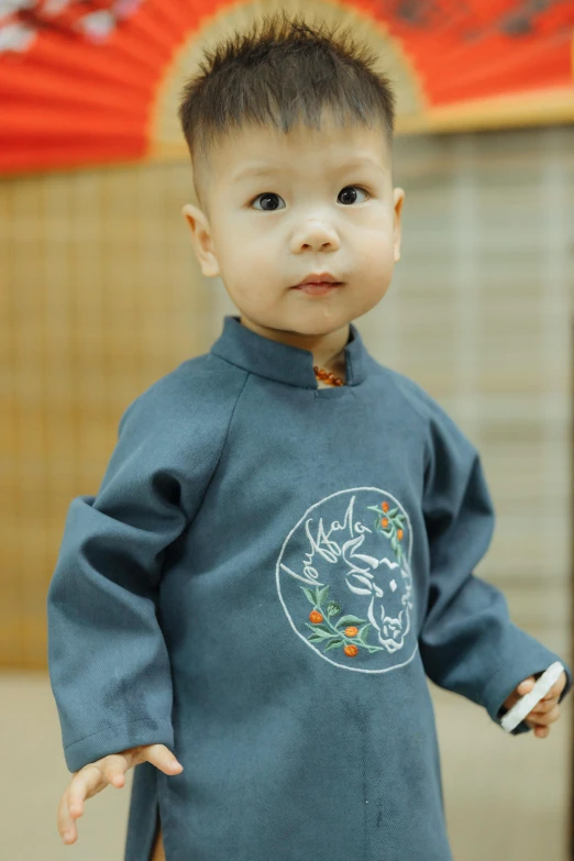 a young boy standing in front of a red umbrella, inspired by Gu An, embroidered shirt, grey, 2 years old, medium close shot