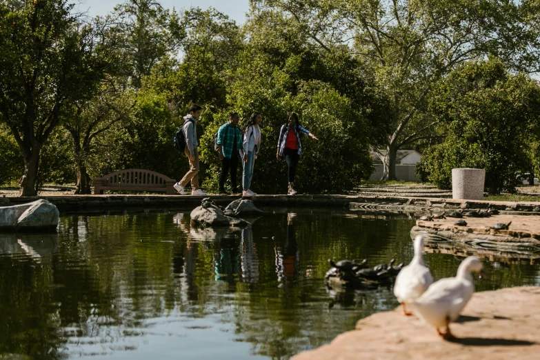 a group of people standing next to a body of water, by Jacob Duck, happening, walking at the garden, college, teals, tourism photography