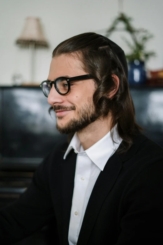 a man with long hair sitting in front of a piano, wearing black rimmed glasses, andrea savchenko, profile image, big smirk