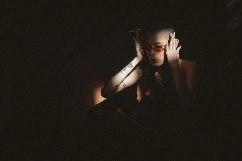 a man sitting in the dark with his hands on his face, a portrait, inspired by Elsa Bleda, pexels, wearing red tainted glasses, portrait of a smoking woman, hairless, bella poarch