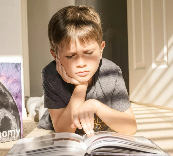 a young boy laying on a bed reading a book, inspired by Leo Leuppi, pexels contest winner, exasperated expression, avatar image, casey cooke, science magazines