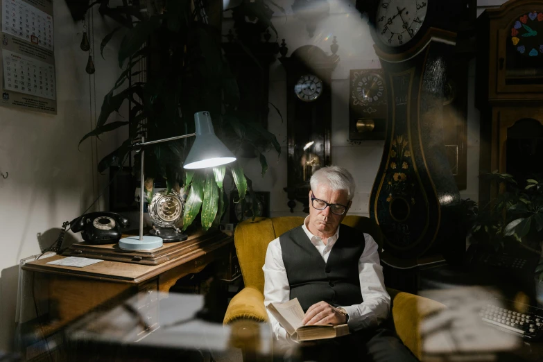 a man sitting in a chair reading a book, a portrait, pexels contest winner, a silver haired mad, low light cinematic, reading glasses, lachlan bailey