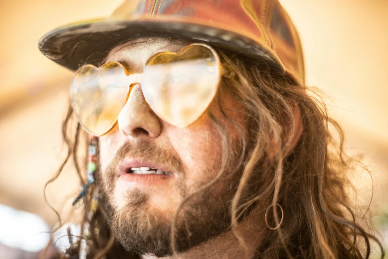 a man with long hair wearing sunglasses and a hat, by Arnie Swekel, unsplash, process art, gold glasses, gnarly details soft light, loving stare, heath clifford