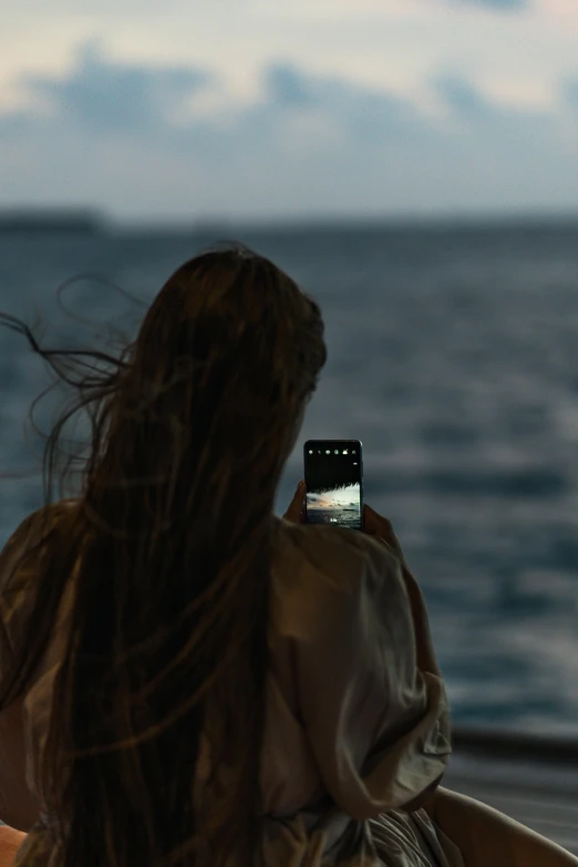 a woman taking a picture of the ocean with her cell phone, by Alexis Grimou, unsplash contest winner, video art, still from a ridley scott movie, on a boat, dark sky, mermaids in distance