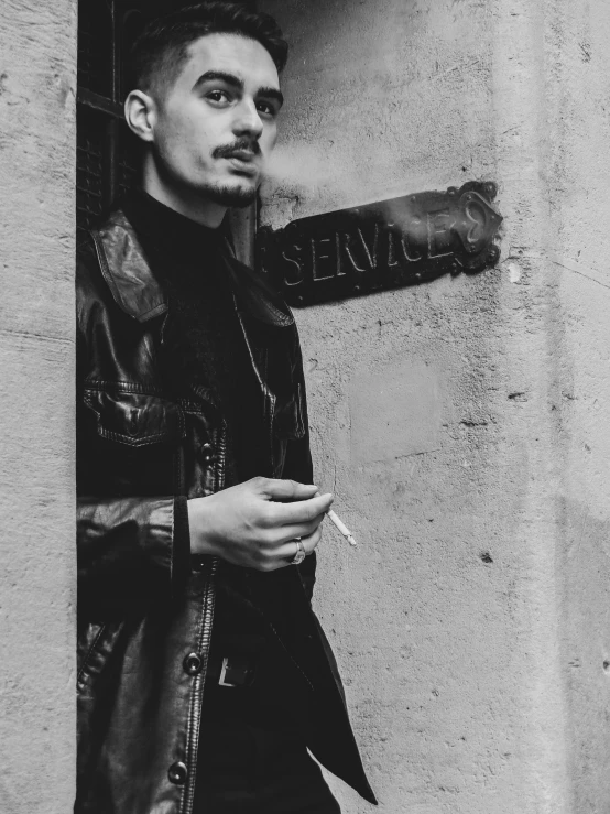 a black and white photo of a man smoking a cigarette, a photo, by Emma Andijewska, wearing a leather trench coat, he got a big french musctache, 35mm!!! 1990, clothed in ancient street wear