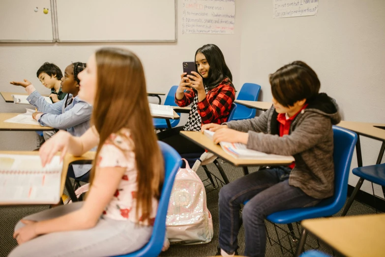 a group of children sitting at desks in a classroom, trending on pexels, she is holding a smartphone, pokimane, profile image, thumbnail