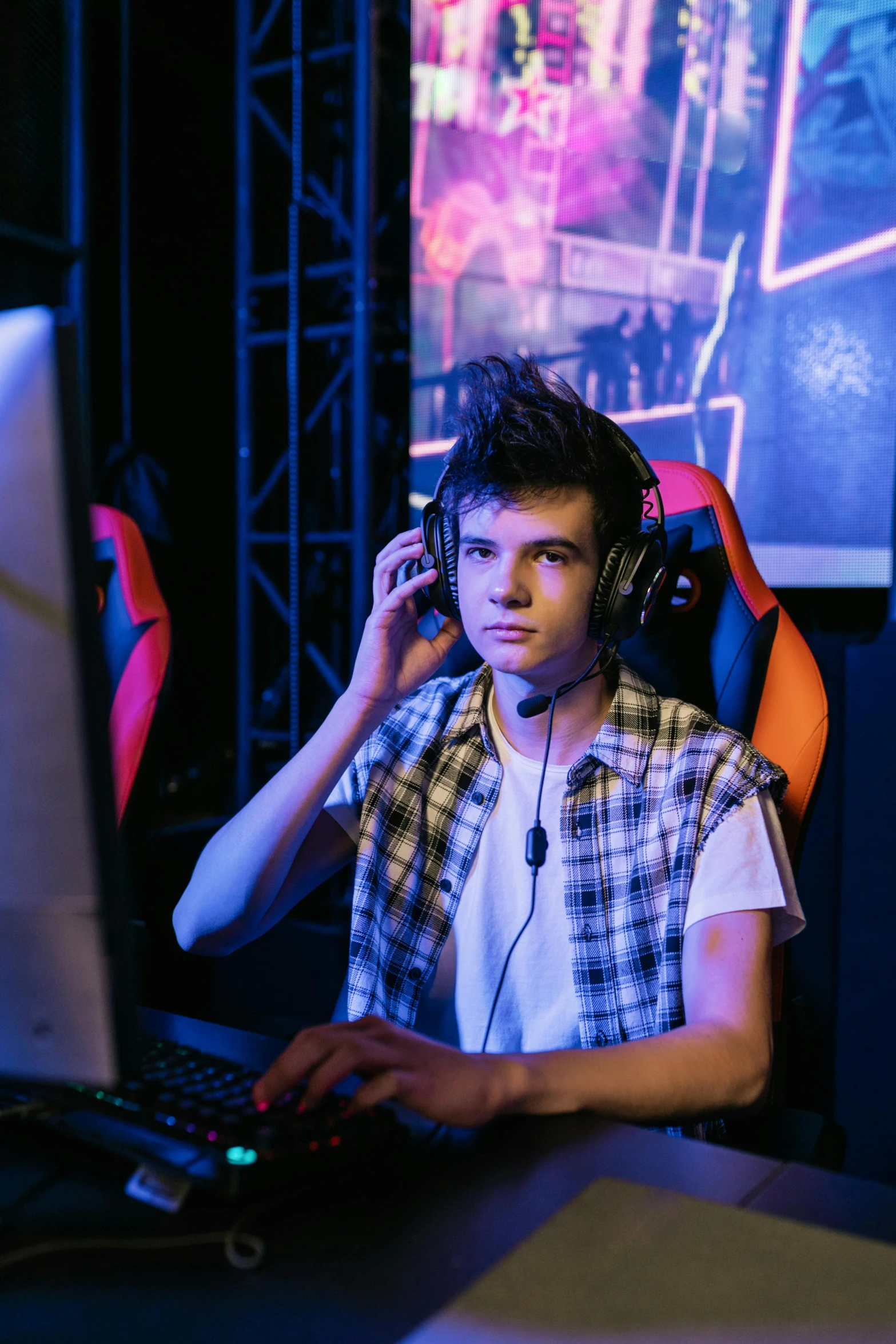 a man sitting in front of a computer with headphones on, a portrait, shutterstock, riot games, 1 6 years old, stern expression, 000