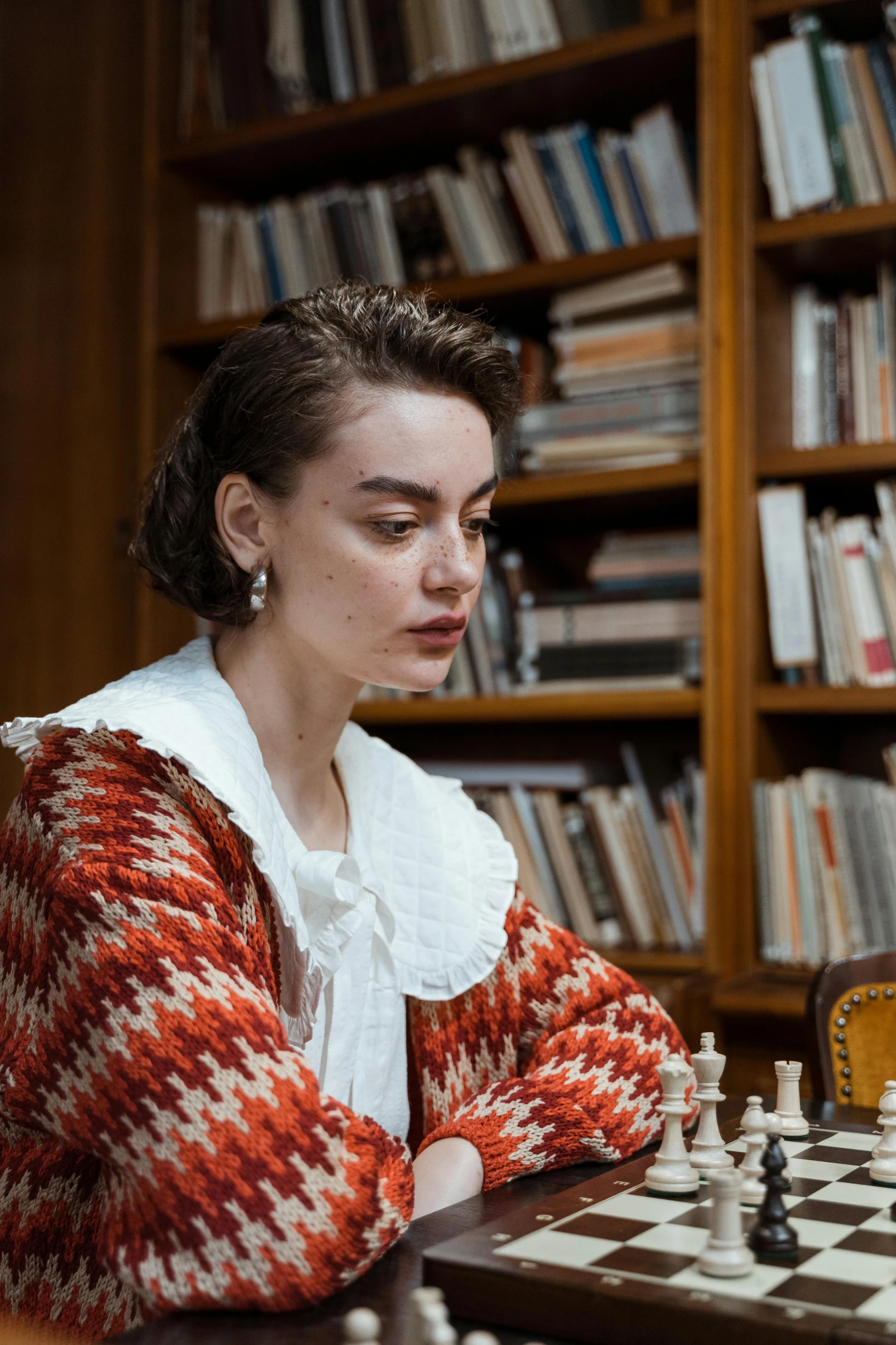 a woman sitting at a table playing a game of chess, a portrait, inspired by Eliseu Visconti, trending on unsplash, wearing a fancy jacket, in a library, film still promotional image, portrait sophie mudd