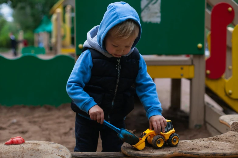 a little boy that is playing with a toy truck, inspired by Myles Birket Foster, pexels contest winner, using a spade, wearing a blue hoodie, digger land amusement park, hand carved