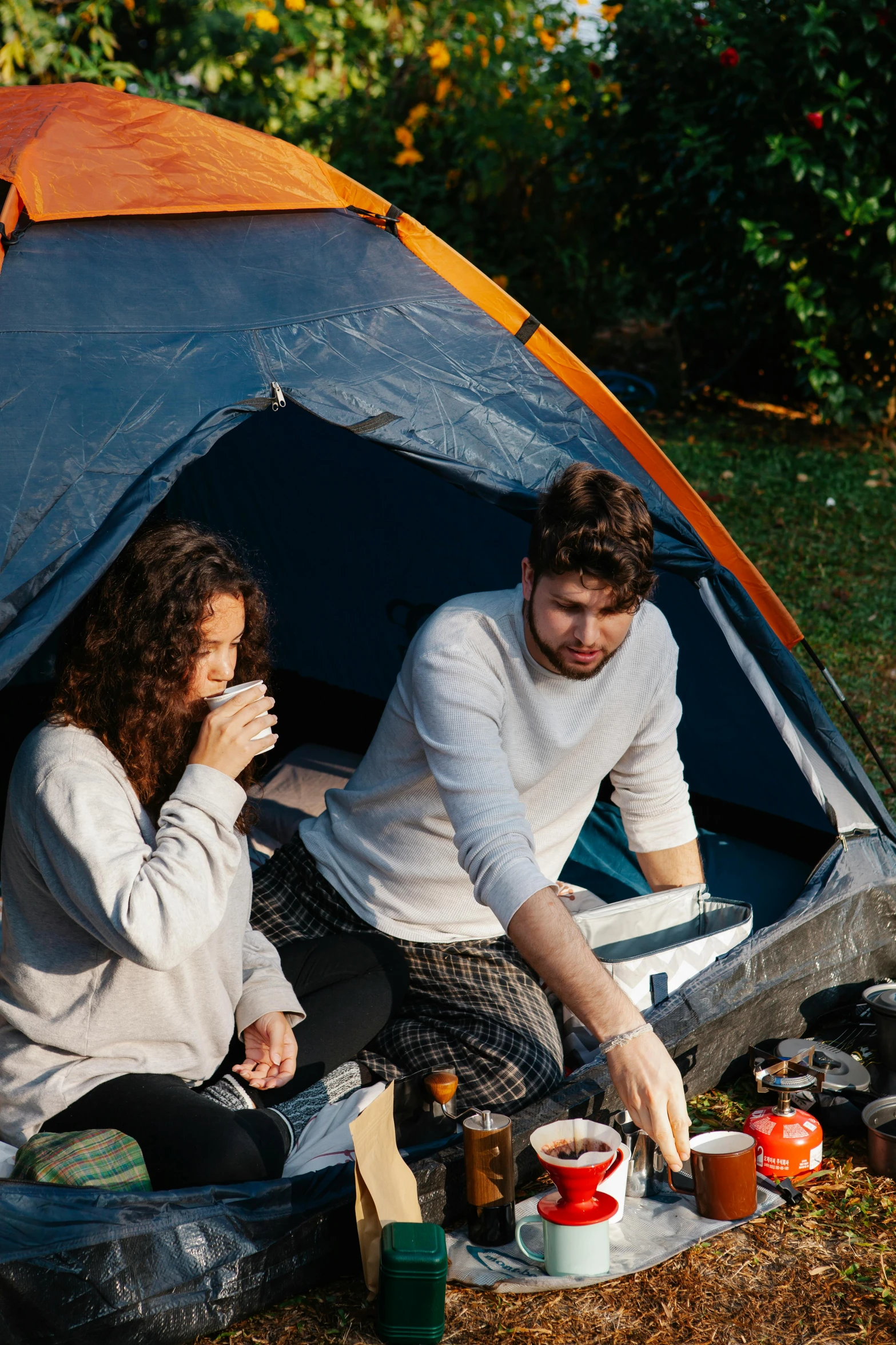 a couple of people sitting in front of a tent, talking, sitting down