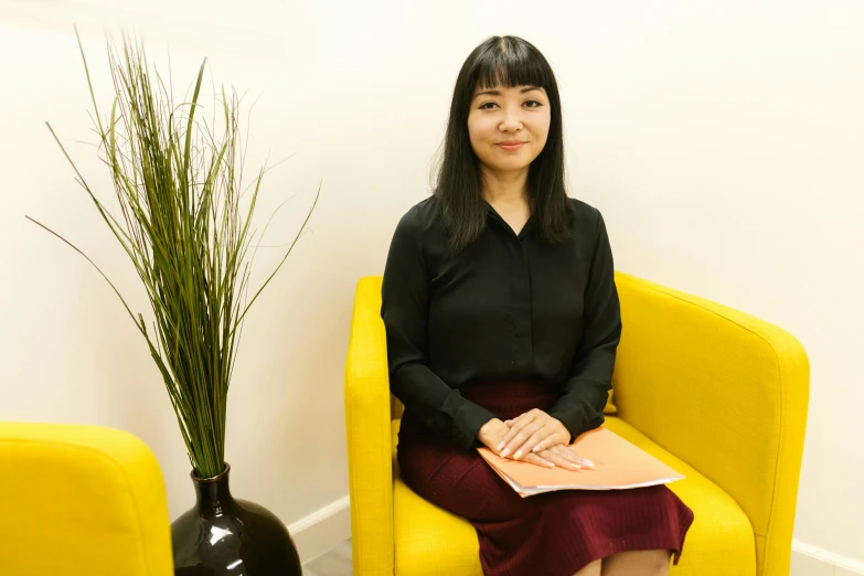 a woman sitting in a yellow chair next to a plant, darren quach, sat in an office, professional profile photo, profile image