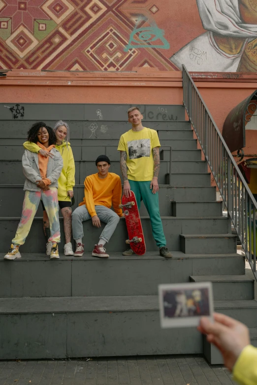 a person taking a picture of a group of people, inspired by Wes Anderson, trending on pexels, graffiti, standing on a skateboard, yellow clothes, promo image, colorful uniforms