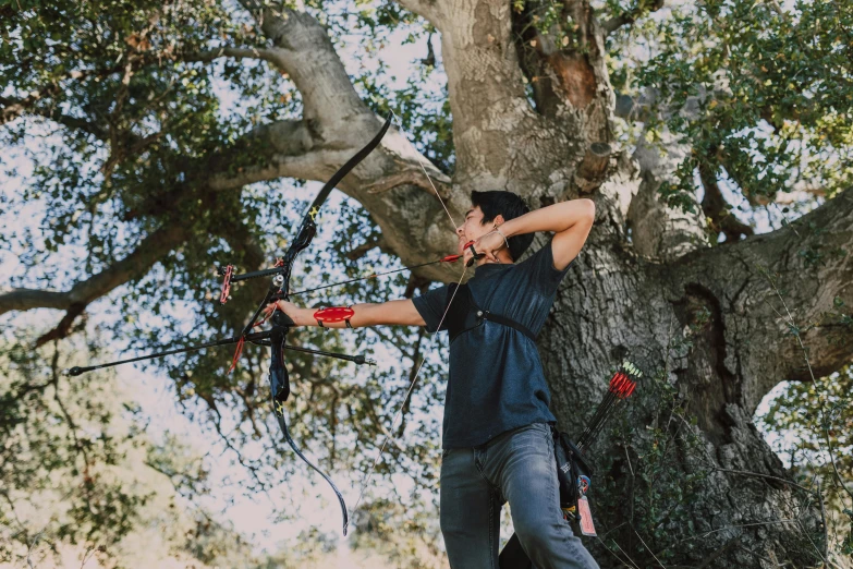 a man holding a bow and arrow in front of a tree, by Meredith Dillman, unsplash, black steel with red trim, bay area, flying trees and park items, gemma chen