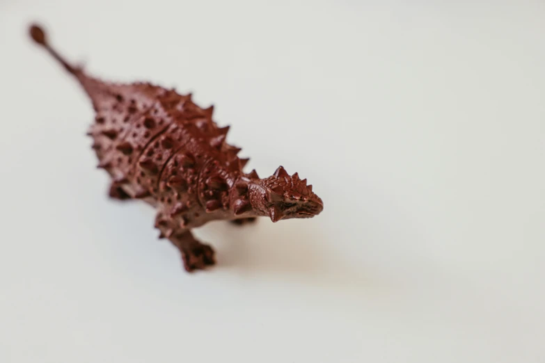 a close up of a toy lizard on a white surface, trending on unsplash, chocolate art, high resolution print :1 red, triceratops, detailed product shot