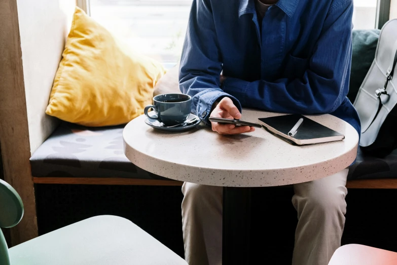 a man sitting at a table with a cup of coffee, trending on unsplash, happening, taken on iphone 14 pro, cafe tables, full body close-up shot, couch desk