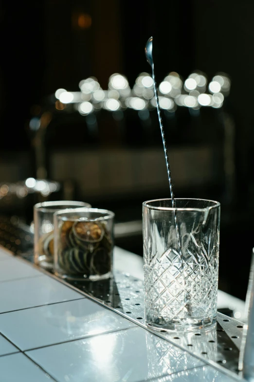 a glass of water sitting on top of a counter, by Richmond Barthé, kinetic art, reflecting light in a nightclub, newton's cradle, silver small glasses, local bar