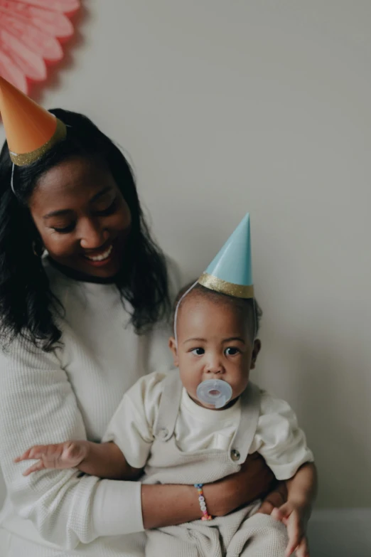 a woman holding a baby wearing a party hat, pexels contest winner, visual art, varying ethnicities, thumbnail, 1 2 9 7, mid shot