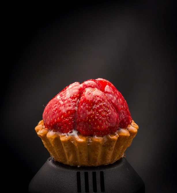 a close up of a pastry with a strawberry on top, by Matthias Stom, unsplash, photorealism, with a black background, symmetrical front view, small crown, coral red