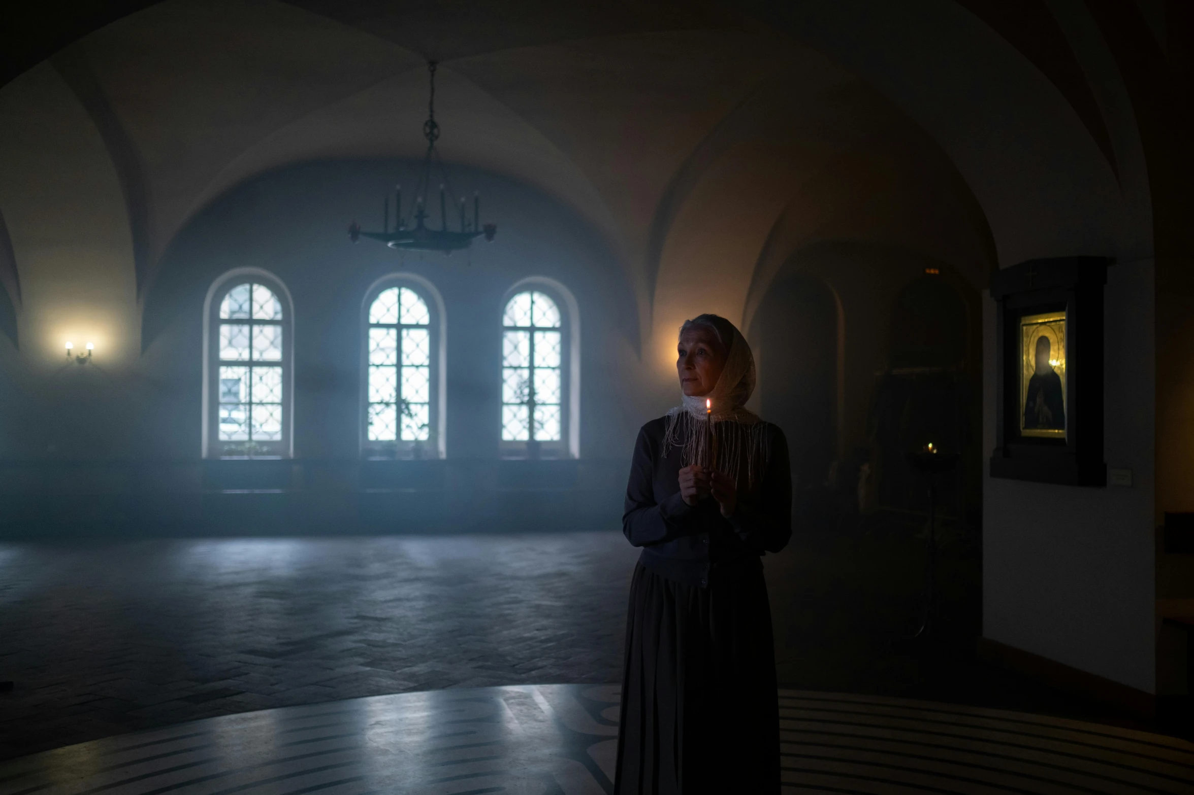 a woman standing in a dark room holding a candle, by Emma Andijewska, baroque, standing inside of a church, tarkovsky scene, set photo in costume, promotional image