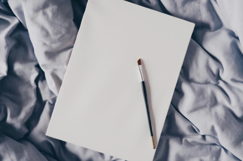 a pen sitting on top of a piece of paper on top of a bed, a minimalist painting, trending on pexels, white cloth, holding a paintbrush, white sketchbook style, thumbnail