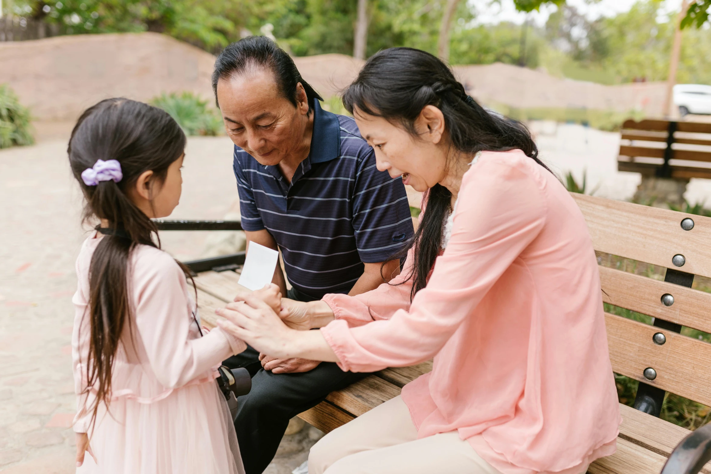 a couple of people that are sitting on a bench, of a family standing in a park, card game, darren quach, blessing hands