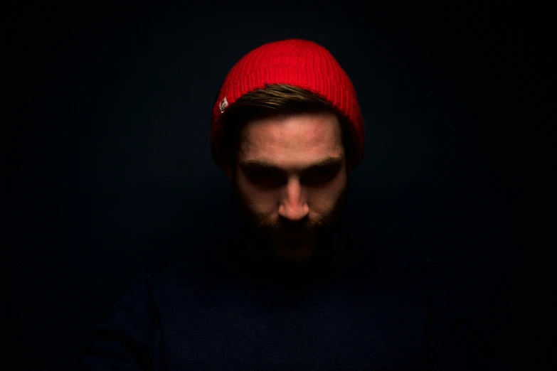 a man with a beard wearing a red hat, a character portrait, unsplash, dark blue beanie, pewdiepie, dramatic product shot, poorly lit