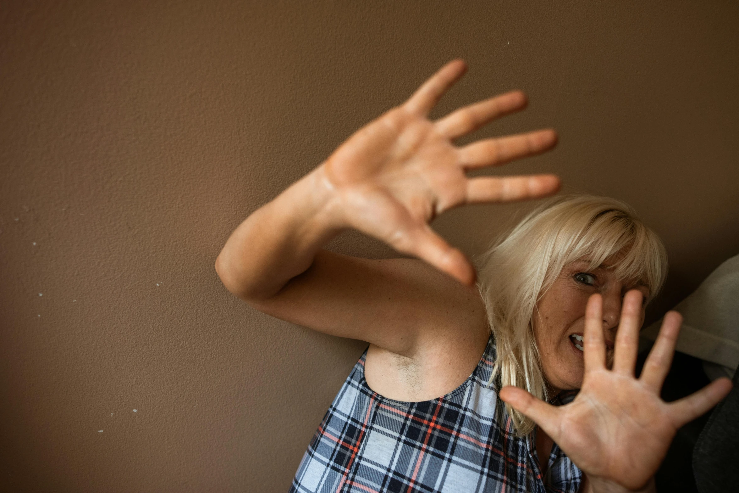 a woman standing in front of a wall with her hands in the air, by Lee Loughridge, pexels, movie still of a snarling, a blond, claustrophobia, hands shielding face