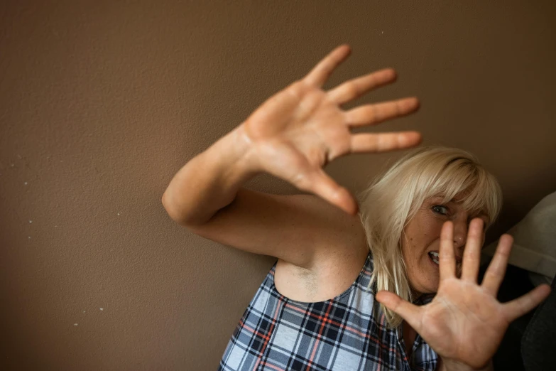a woman standing in front of a wall with her hands in the air, by Lee Loughridge, pexels, movie still of a snarling, a blond, claustrophobia, hands shielding face