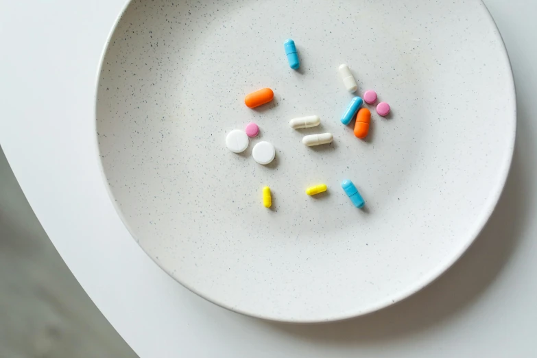 a white plate topped with different colored pills, unsplash, antipodeans, shot on sony a 7, frank moth, cast, biotech