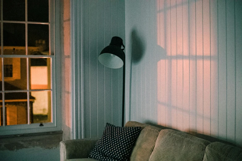 a couch sitting in a living room next to a window, inspired by Elsa Bleda, pexels contest winner, emerging from a lamp, poorly lit, lantern light besides, soft light through blinds