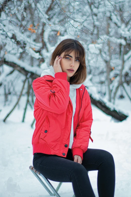 a woman sitting on a chair in the snow, a colorized photo, pexels contest winner, wearing a bomber jacket, coral red, mia khalifa, portrait mode photo