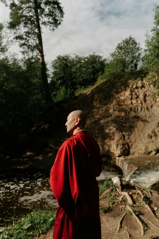 a man in a red robe standing in front of a waterfall, unsplash, renaissance, ukrainian monk, on a riverbank, portrait of bald, profile pic