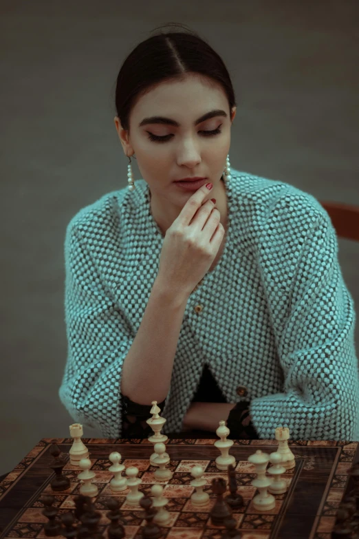 a woman sitting at a table playing a game of chess, a colorized photo, inspired by Elsa Bleda, trending on unsplash, synthetism, wearing a fancy jacket, portrait of gal gadot, high fashion photoshoot, sad look