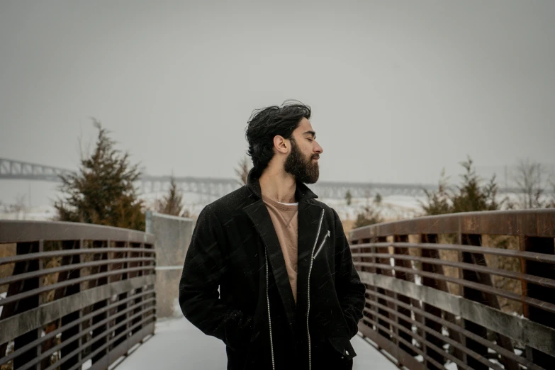 a man with a beard standing on a bridge, by Marshall Arisman, pexels contest winner, only snow i the background, riyahd cassiem, with a beard and a black jacket, nekro petros afshar