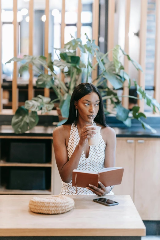 a woman sitting at a table reading a book, pexels contest winner, happening, iced latte, with brown skin, confident looking, inspect in inventory image