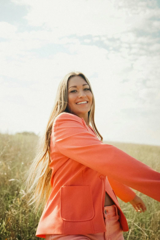 a woman standing in a field holding a frisbee, pexels contest winner, color field, long hair and red shirt, orange jacket, turning her head and smiling, large)}]