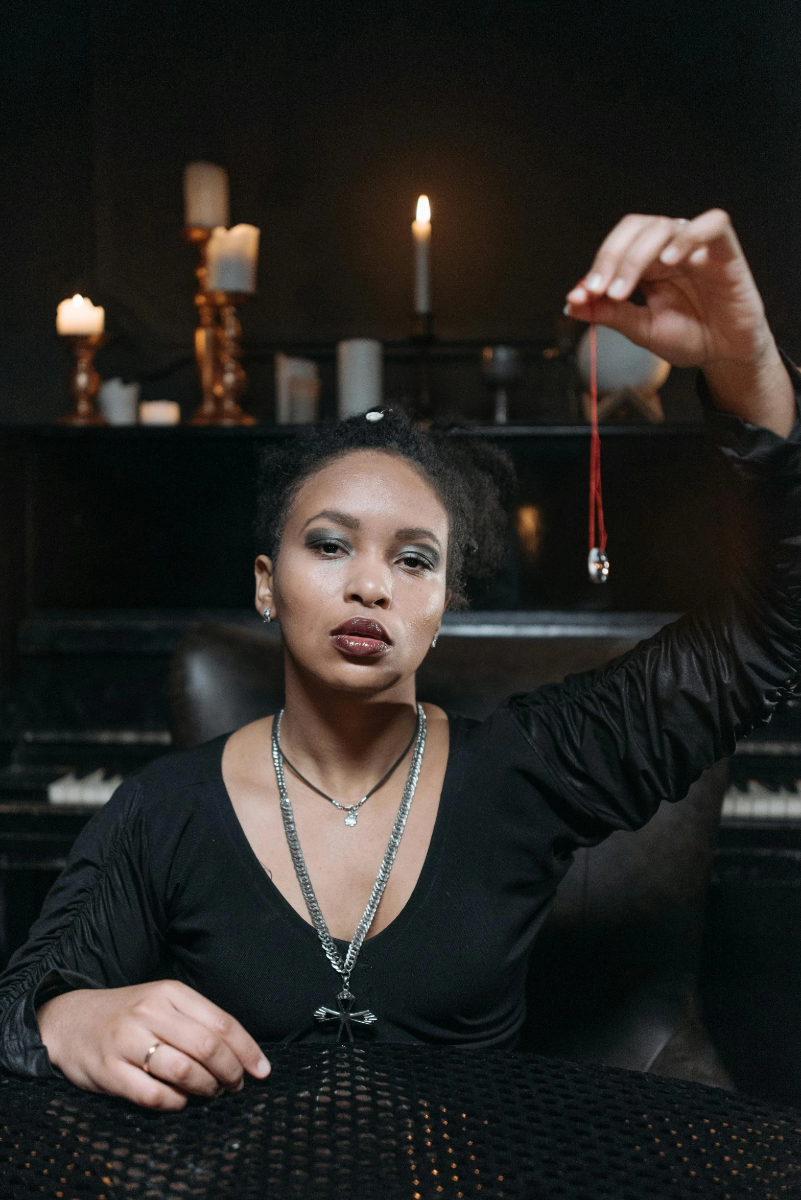 a woman sitting at a table in front of a piano, a portrait, trending on pexels, black arts movement, an arcane wizard casting a spell, wearing several pendants, promotional photo, holding a magic needle