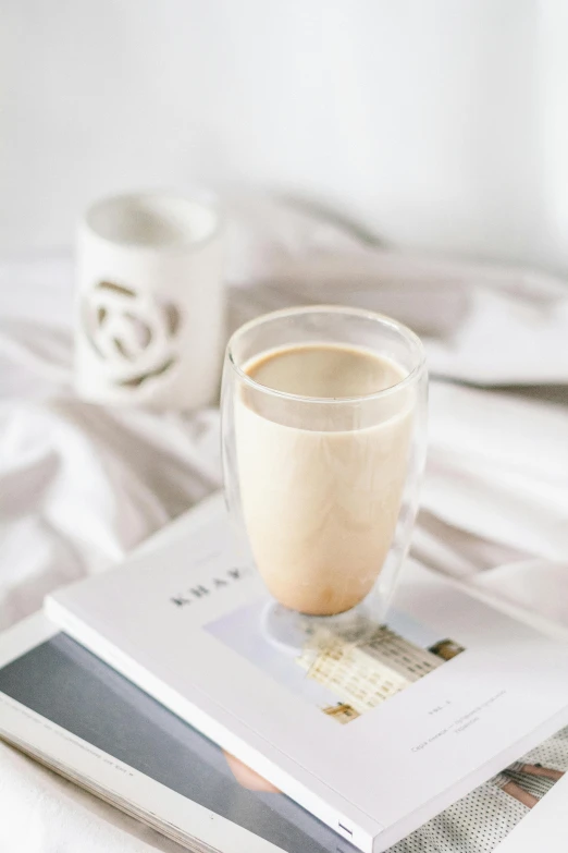 a book sitting on top of a bed next to a cup of coffee, vanilla smoothie explosion, thumbnail, glassware, beige