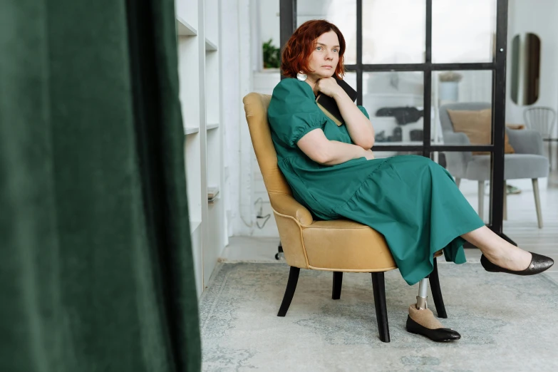 a woman in a green dress sitting in a chair, by Emma Andijewska, pexels, teal tunic, redhead woman, surgical gown and scrubs on, pondering