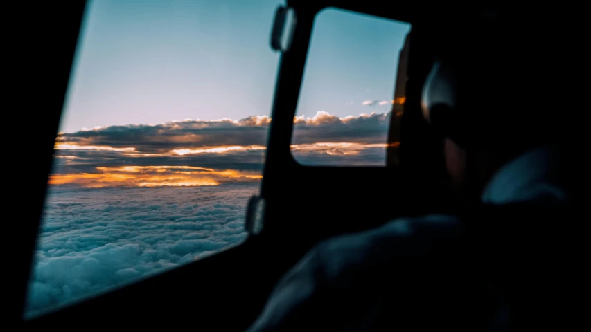 a man looks out the window of a plane as the sun sets, pexels contest winner, hurufiyya, inside of a car, view from helicopter, through clouds blue sky, late summer evening